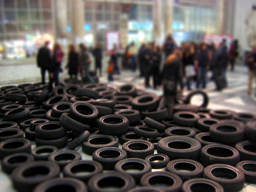 Dozens of tires lined up on the ground, with people in the background.