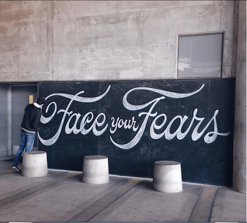 Scott Biersack working on a big wall with the hand letterring that states: face your fears