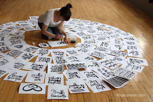 Kal Barteski is surrounded by many sheets of hand lettering on the floor.