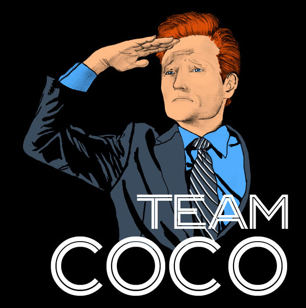 Conan in a suit and tie, blue shirt with sign saying Team Coco, on a black background