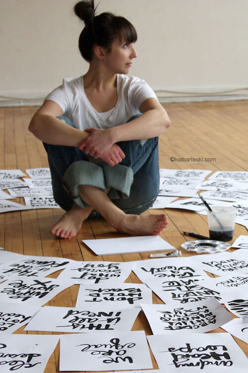 Kal Barteski is surrounded by many sheets of hand lettering on the floor.